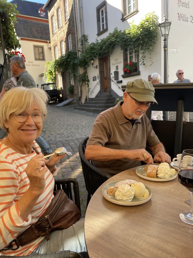 To personer nyter desserter utendørs i en koselig gate, med en kopp kaffe og et glass vin på bordet.
