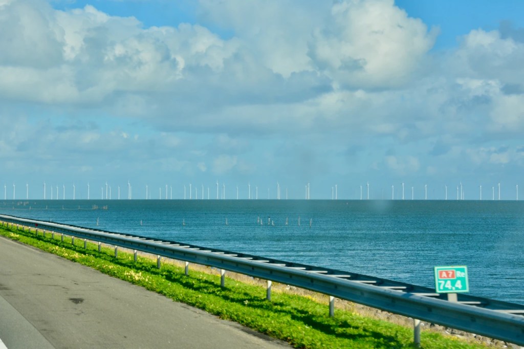 Utsikt over havet med vindmøller i bakgrunnen og en vei langs kysten.