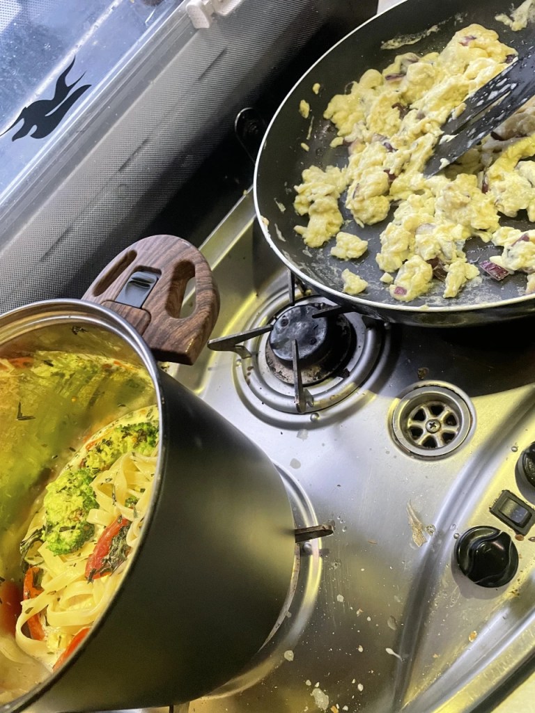 Kjøkkenbilde med en gryte med pasta og grønnsaker til venstre og en stekepanne med egg til høyre.