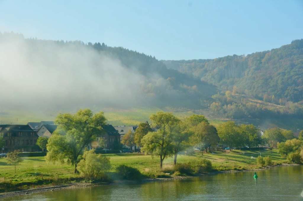 Utsikt over elven med tåke og frodige åser i bakgrunnen.