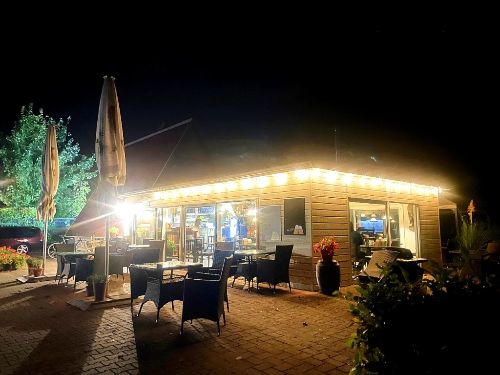 Bilde av en koselig restaurant med utendørs sitteplasser, opplyst av lys i taket, tatt om natten.