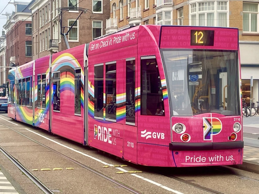 En rosa sporvogn dekorert med regnbuefarger, som promoterer Pride, med teksten 'Pride with us' synlig.
