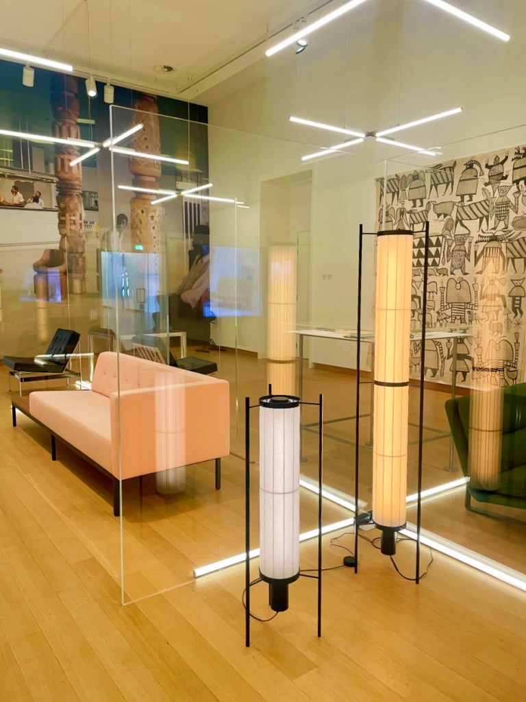 Moderne innredning i et rom med glassvegger, inkludert en rosa sofa, dekorative lampestativer og kunstverk på veggene.