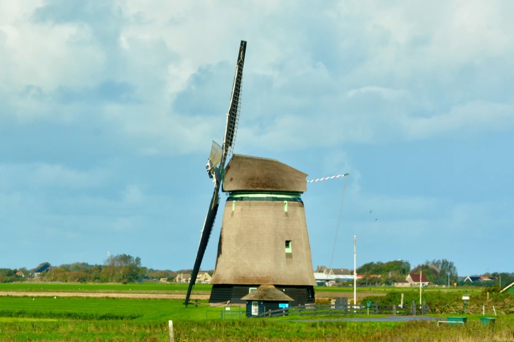 En tradisjonell vindmølle i et flatt landskap med grønne marker og en blå himmel.